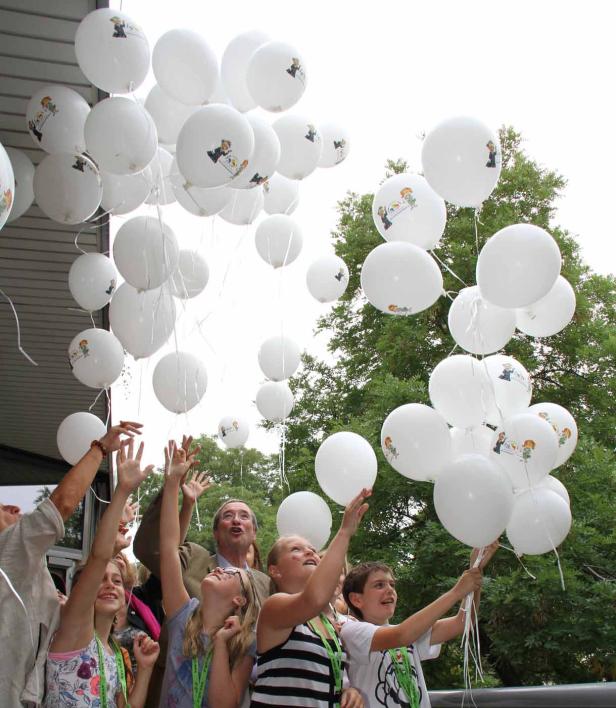 Eine Gruppe von Menschen lässt weiße Ballons mit einer Abbildung in den Himmel steigen.