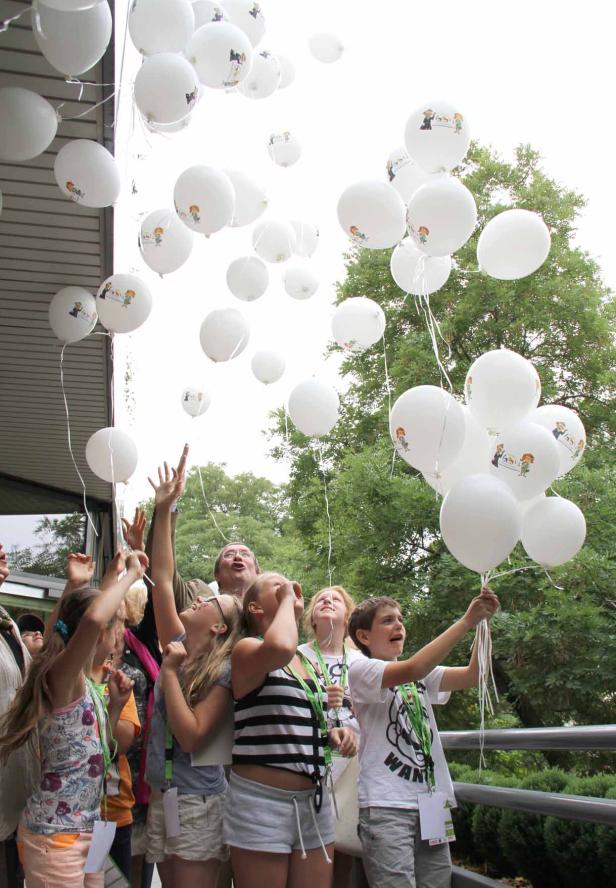 Eine Gruppe Kinder lässt weiße Ballons mit Zeichnungen in den Himmel steigen.