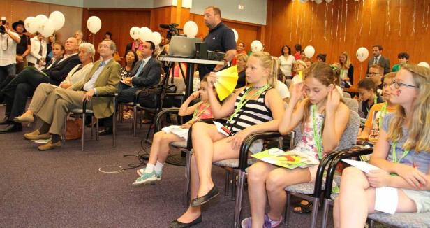 Eine Gruppe von Menschen, darunter viele Kinder, sitzt in einem Raum mit weißen Luftballons.
