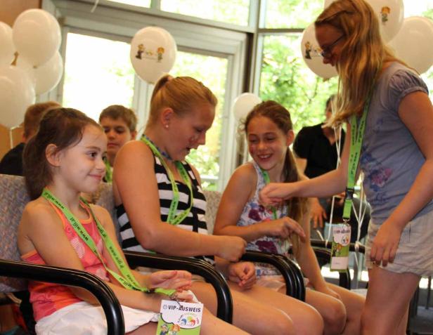Mehrere Mädchen sitzen auf Stühlen und unterhalten sich, einige tragen VIP-Ausweise.