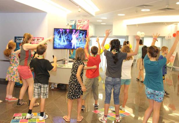 Eine Gruppe Kinder tanzt vor einem Bildschirm, auf dem ein Tanzspiel läuft.