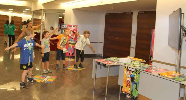 Eine Gruppe Kinder tanzt zu „Just Dance“ unter Anleitung einer Frau.