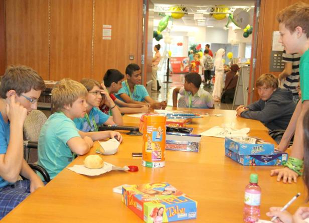 Eine Gruppe Kinder sitzt an einem Tisch mit Spielen wie Tabu Junior.