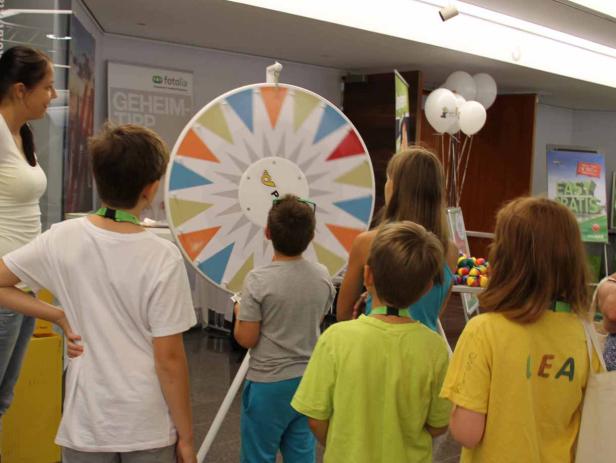 Kinder stehen um ein Glücksrad mit bunten Dreiecken.