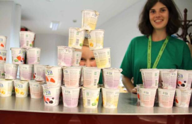 Eine Frau steht hinter einem Tisch mit gestapelten Joya-Joghurts.