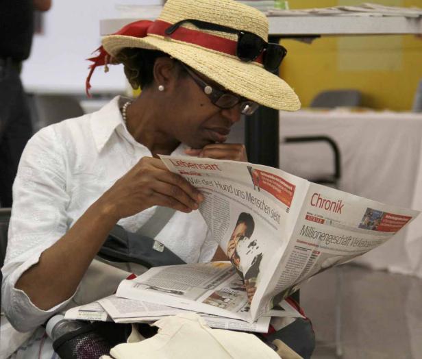 Eine Frau mit Hut und Brille liest eine Zeitung.