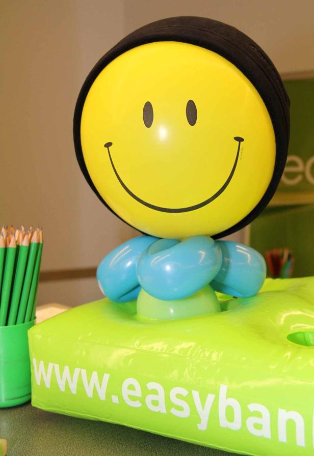 Ein gelber Smiley-Ballon mit schwarzer Mütze auf einem grünen Werbeartikel von Easybank.