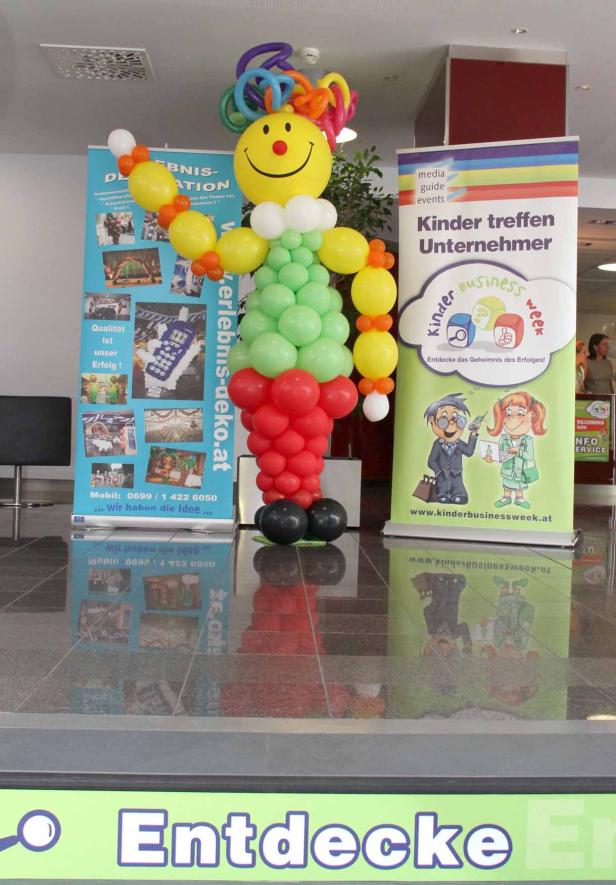 Ein Ballon-Clown steht neben einem Werbebanner für die Kinder Business Week.
