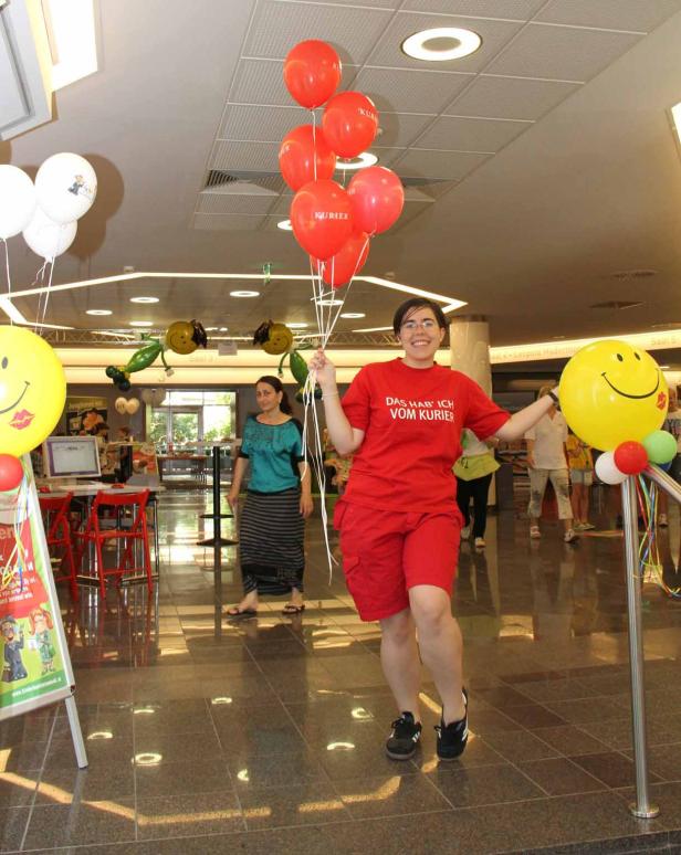 Eine Frau mit roten Luftballons und einem roten T-Shirt mit der Aufschrift „Das hab ich vom Kurier“.
