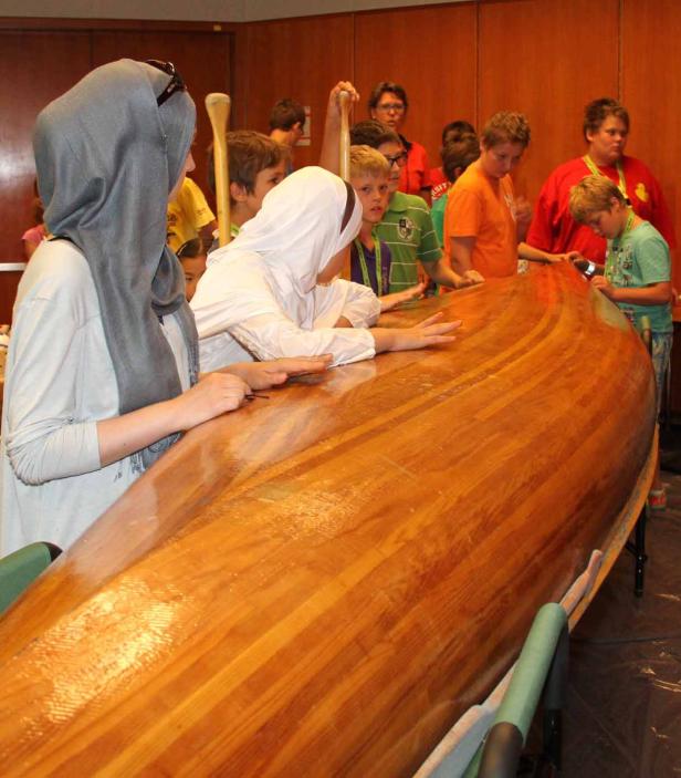 Eine Gruppe von Kindern betrachtet ein hölzernes Kanu.