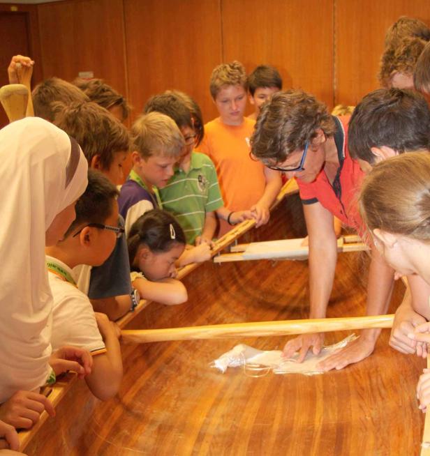 Eine Gruppe von Kindern und ein Erwachsener arbeiten an einem Holzboot.