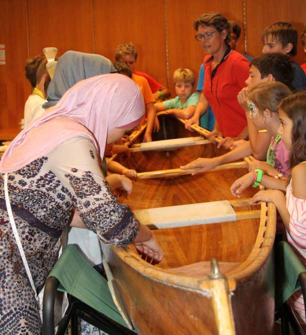 Eine Gruppe von Kindern und eine Frau betrachten ein hölzernes Kanu.