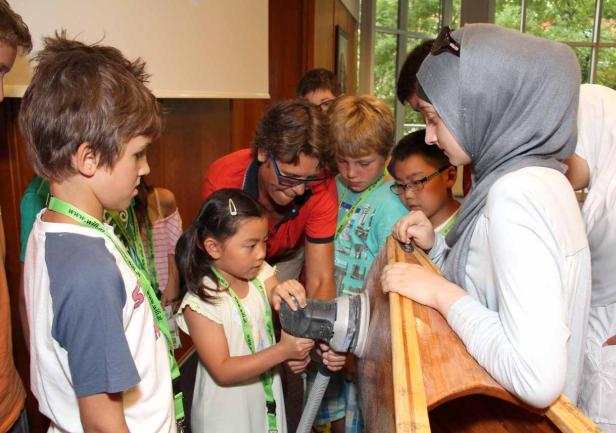 Eine Gruppe von Kindern schleift unter Aufsicht ein Holzboot.
