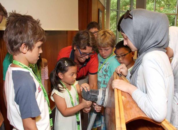 Eine Gruppe Kinder schleift unter Aufsicht ein Holzboot.