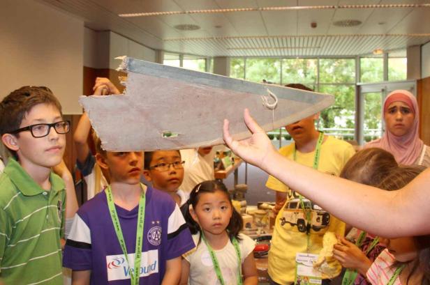 Eine Gruppe Kinder betrachtet ein beschädigtes Flugzeugteil.