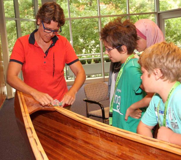 Eine Frau arbeitet an einem Holzboot, während Kinder zusehen.