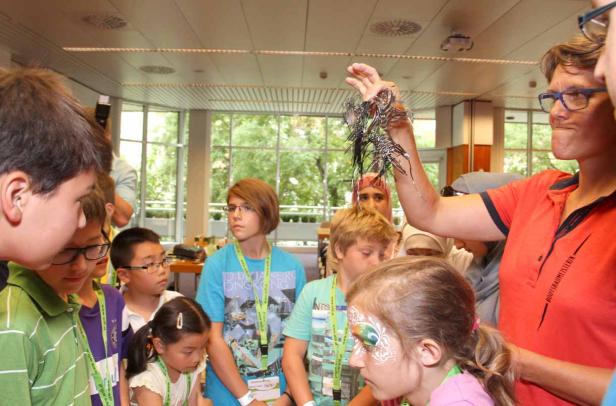 Eine Gruppe Kinder betrachtet aufmerksam eine Dekoration, die eine Frau hochhält.