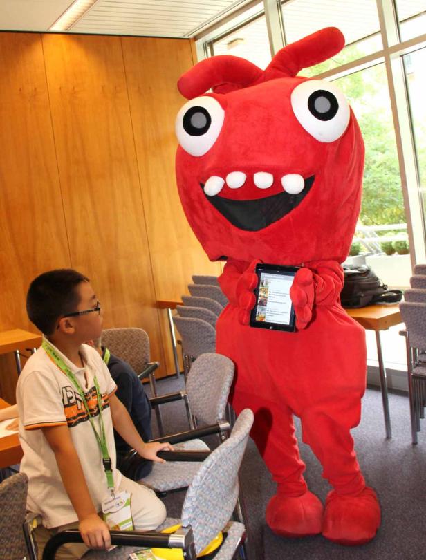 Ein Junge sitzt neben einem roten Monsterkostüm, das ein Tablet hält.
