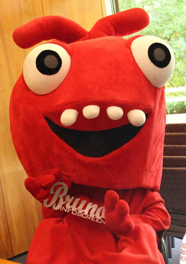Das rote Maskottchen „Bruno Infoscreen“ lächelt mit großen Augen und hervorstehenden Zähnen.