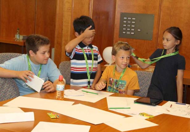 Vier Kinder sitzen an einem Tisch und zeichnen oder basteln.