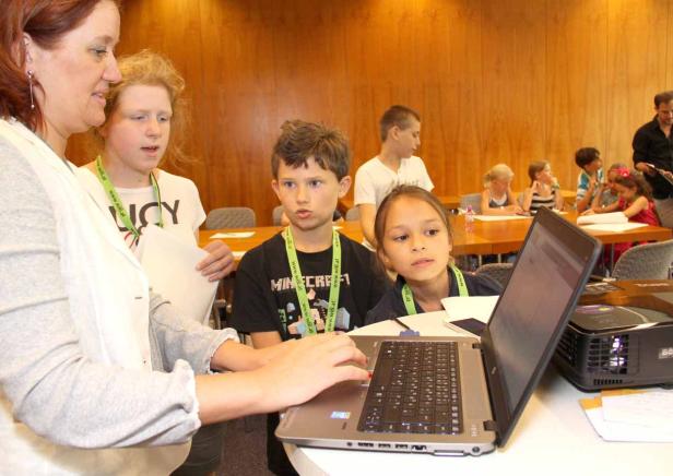 Eine Frau hilft Kindern bei der Arbeit an einem Laptop in einem Klassenzimmer.
