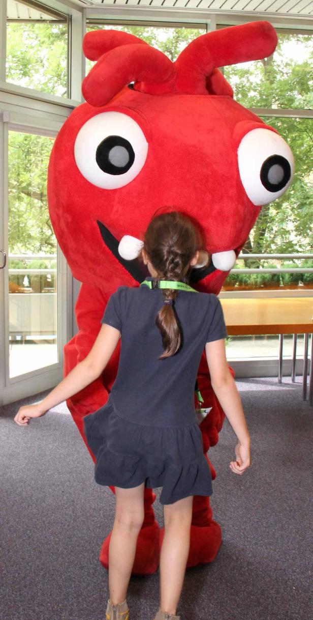 Ein Mädchen umarmt ein großes, rotes Monsterkostüm mit Kulleraugen.