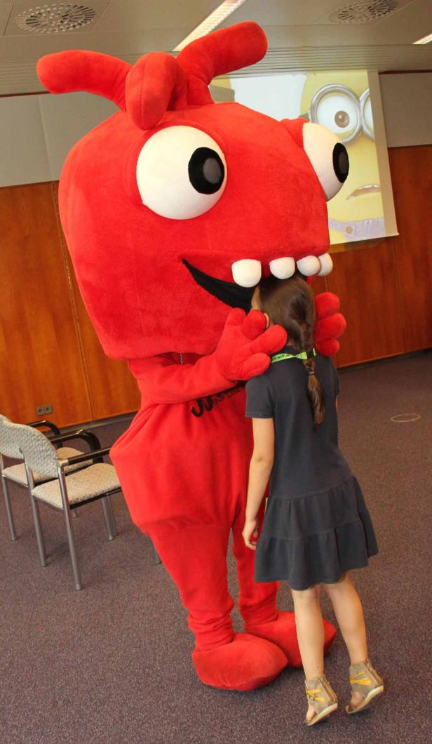 Ein Mädchen umarmt ein großes, rotes Monster-Maskottchen.