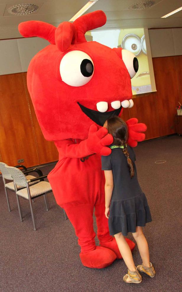 Ein Mädchen umarmt ein rotes, zahniges Monster-Maskottchen.