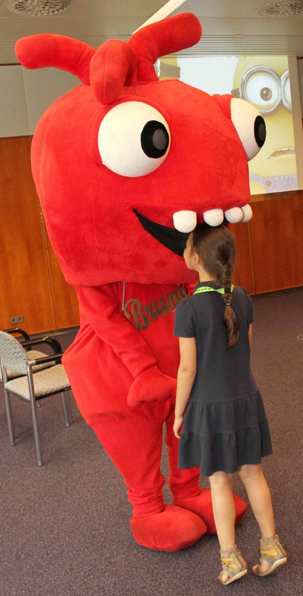 Ein Mädchen steht vor einem großen, roten Maskottchen mit dem Namen „Bruno“.