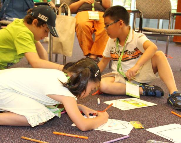 Drei Kinder sitzen auf dem Boden und malen mit Stiften auf Papier.