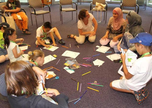 Eine Gruppe von Kindern und eine Frau sitzen im Kreis auf dem Boden und basteln.