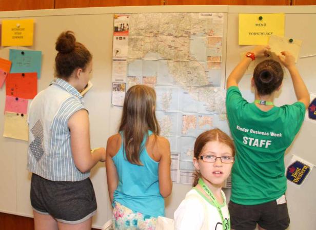 Kinder betrachten eine Italienkarte und Menüvorschläge an einer Wand während der Kinder Business Week.