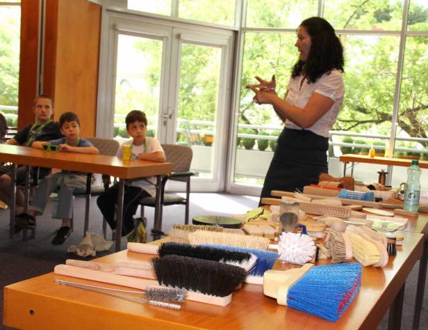 Eine Frau erklärt einer Gruppe von Kindern verschiedene Bürsten.