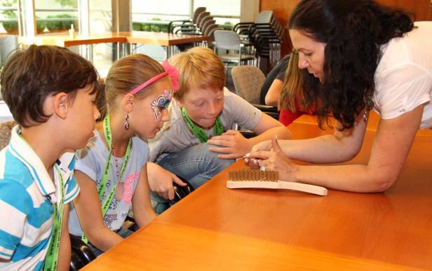 Eine Frau zeigt drei Kindern einen Trick mit einer Bürste auf einem Tisch.