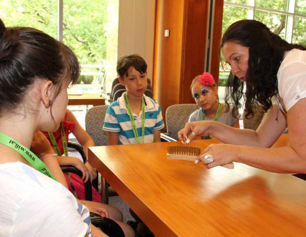 Eine Frau zeigt Kindern einen Pinsel an einem Tisch.