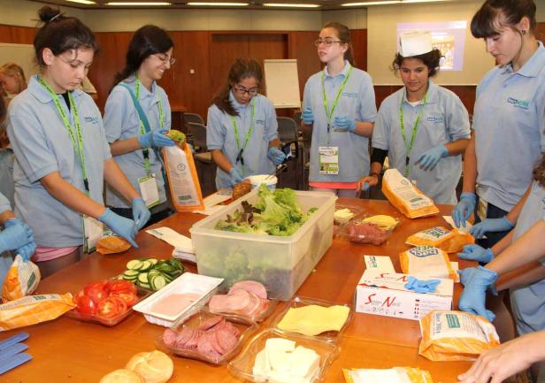 Eine Gruppe von Jugendlichen bereitet belegte Brote mit Salat, Wurst und Käse zu.