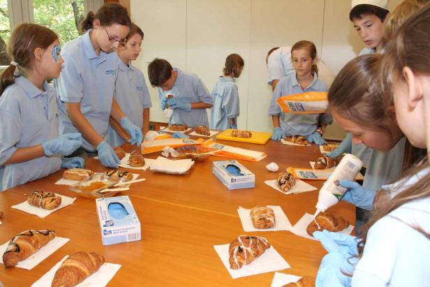 Eine Gruppe Kinder verziert Croissants mit Glasur an einem Tisch.