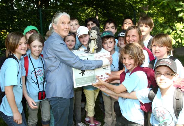Jane Goodall umgeben von Kindern, die eine „Handy-Sammelbox“ halten.