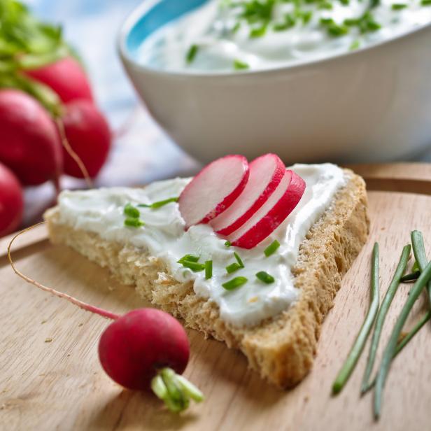 Ein Brot mit Frischkäse, Radieschen und Schnittlauch auf einem Holzbrett.