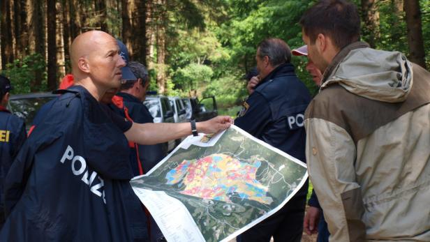 Polizisten besprechen eine farbige Karte in einem Waldgebiet.