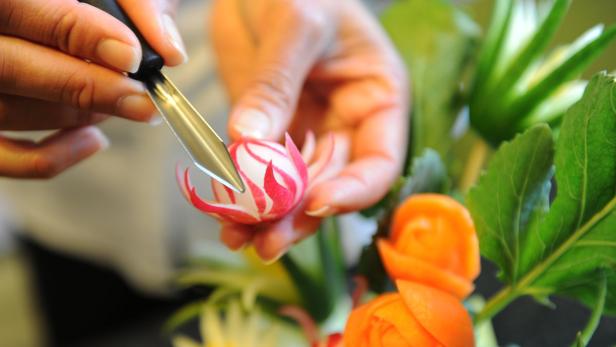 Eine Person schnitzt mit einem Messer eine Radieschenblume.