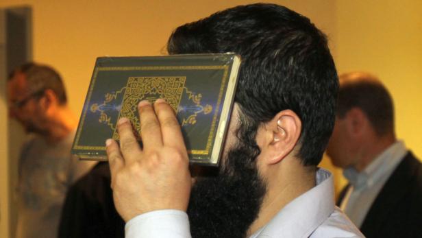 Ein Mann mit Bart hält ein Buch mit islamischen Mustern vor sein Gesicht.