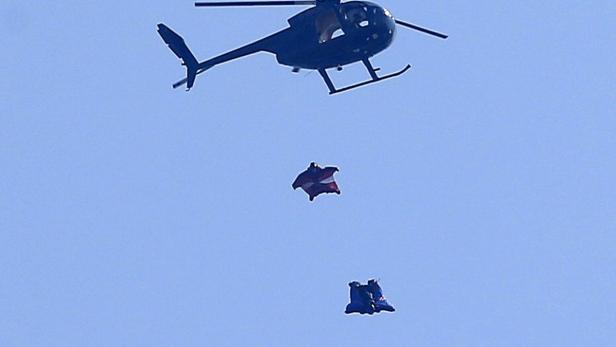Ein Hubschrauber über zwei Wingsuit-Springern vor blauem Himmel.