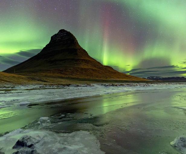Nordlichter über dem Kirkjufell Berg in Island spiegeln sich im Wasser.