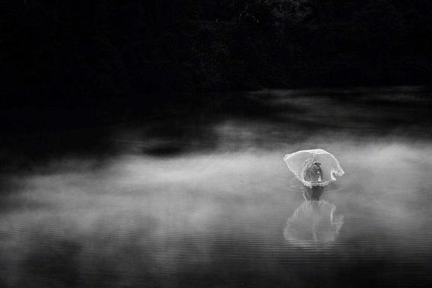 Ein Fischer steht mit einem Netz im nebligen Wasser.