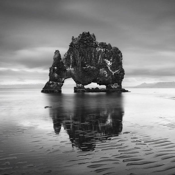 Der Hvítserkur-Felsen, ein Basaltfelsen im Wasser vor Island, spiegelt sich im nassen Sand.