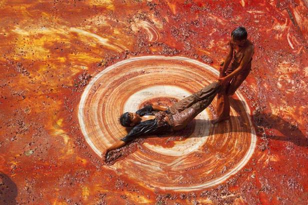 Zwei Männer sind mit roter Farbe bedeckt, einer liegt in einem Farbwirbel.