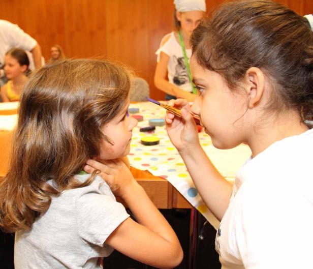 Ein Mädchen bemalt das Gesicht eines anderen Mädchens mit einem Pinsel.