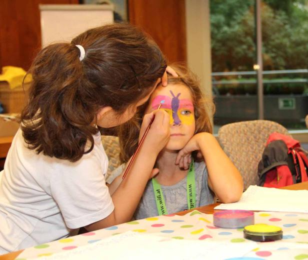 Ein Mädchen bekommt ein Schmetterlingsgesicht von einem anderen Mädchen geschminkt.