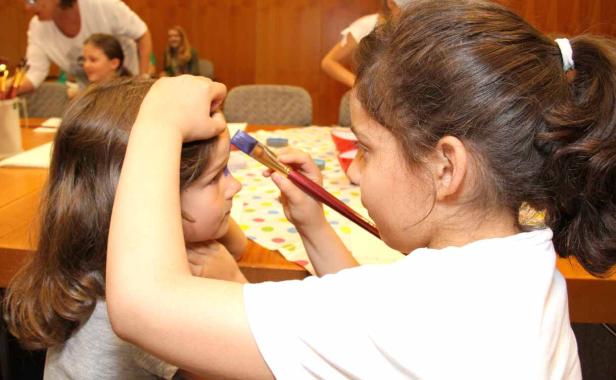 Ein Mädchen bemalt das Gesicht eines anderen Mädchens mit einem Pinsel.